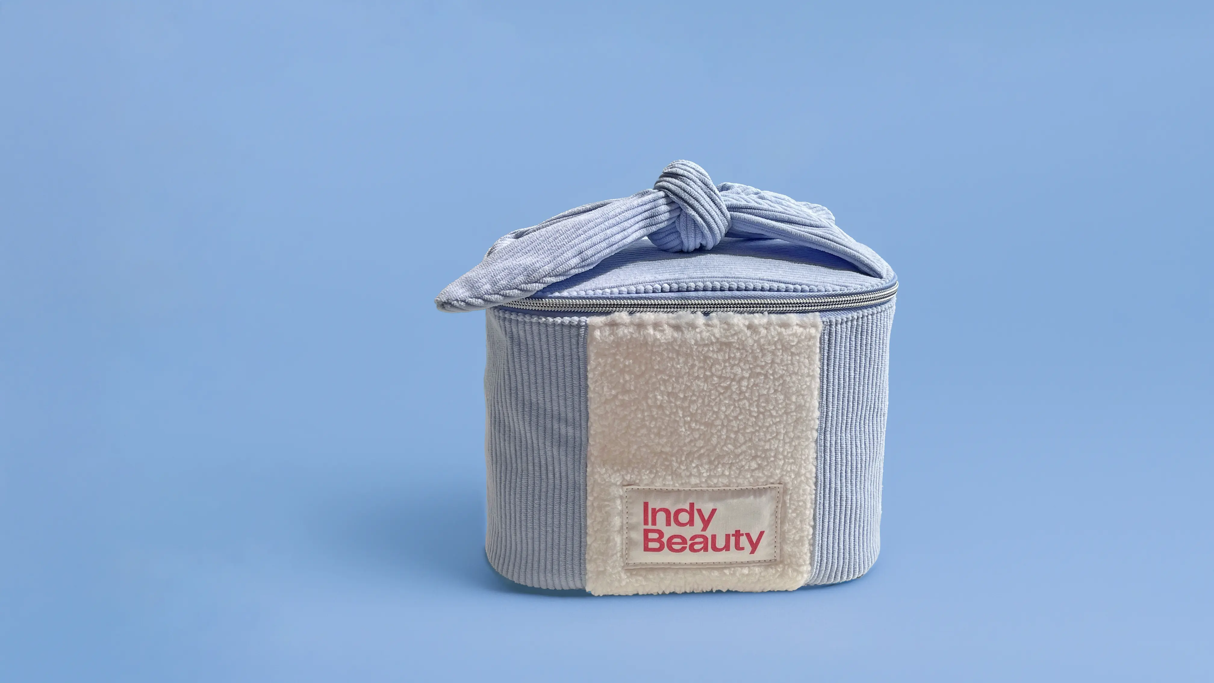 light blue textured cosmetic bag with cream patch & 'Indy Beauty' logo, tied with a matching ribbon