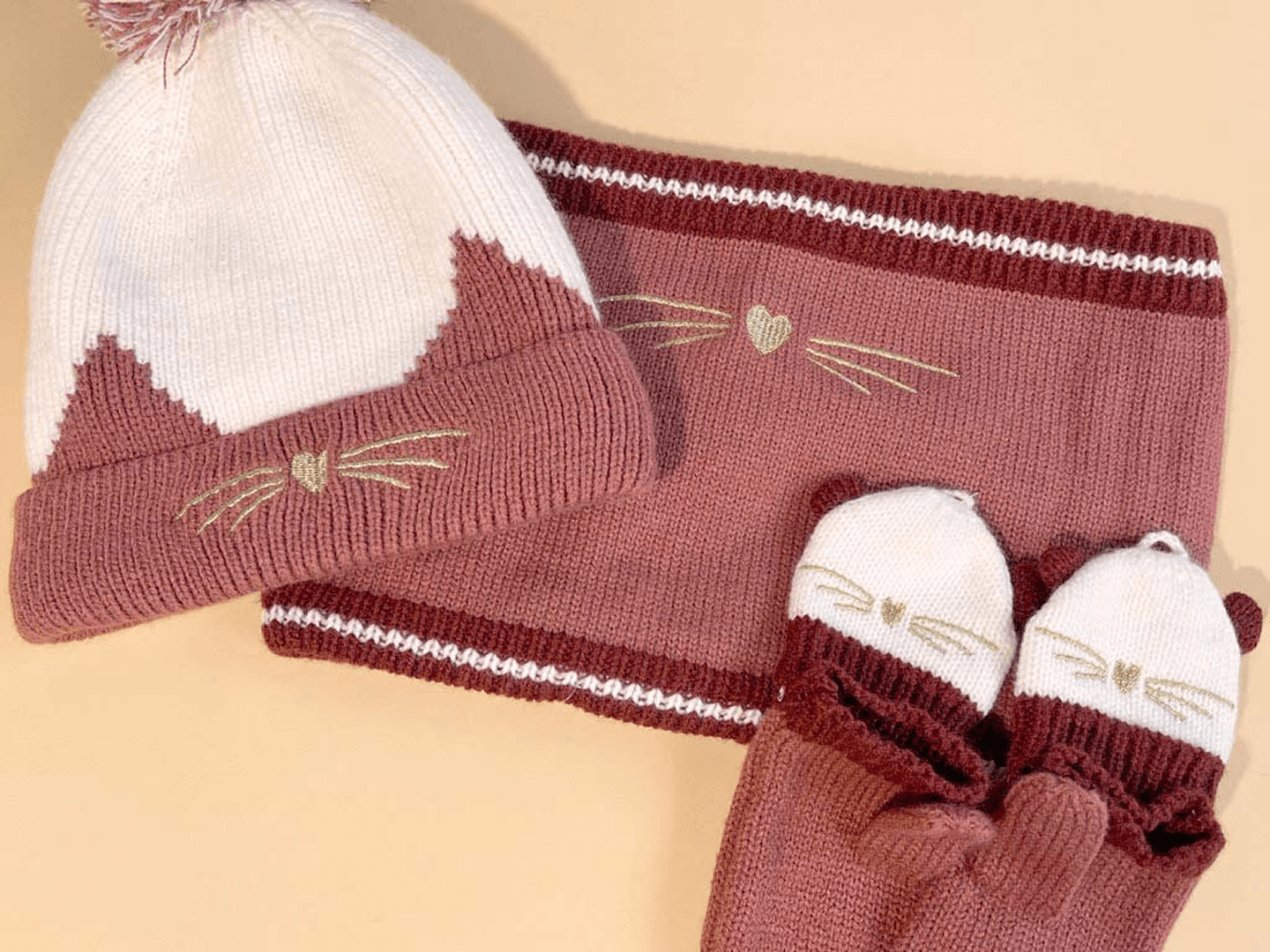 A cozy knit set consisting of a hat, scarf, and mittens adorned with cute cat features, representing Vertbaudet products